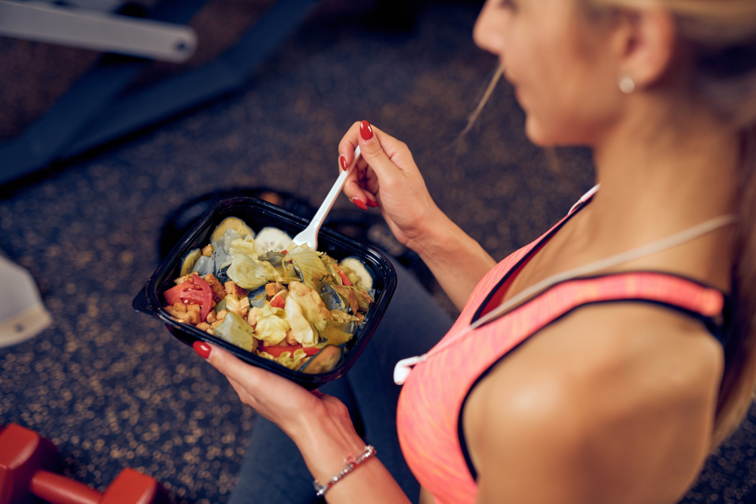 Top view of woman eating healthy food while sitting in a gym. Heatlhy lifestyle concept.